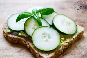 A finished slice of Avocado Toast With Cucumber on a wood surface.