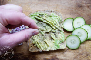 Sprinkling pepper over smashed avocado on a slice of whole grain bread.
