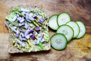 Onions sprinkled over smashed avocado on a slice of whole grain bread.