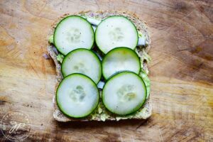 Cucumbers added to onions and smashed avocado on a slice of whole grain bread.