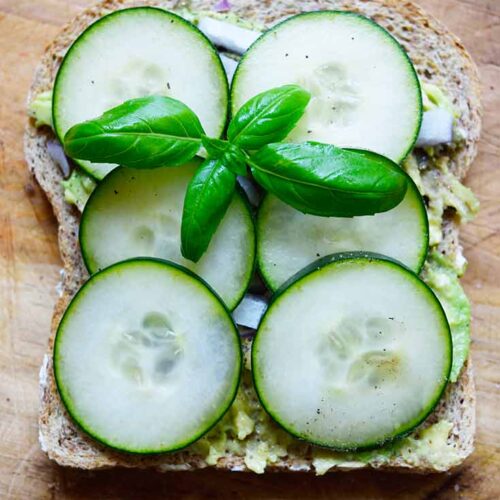 An overhead view of a single slice of Avocado Toast With Cucumber, garnished with a basil leaf.