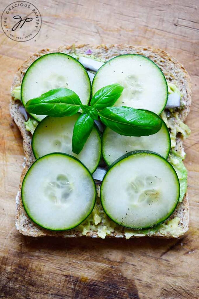An overhead view of a single slice of Avocado Toast With Cucumber, garnished with a basil leaf.
