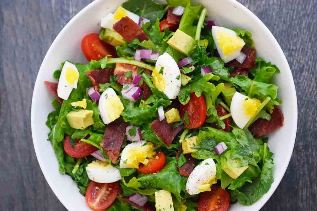 An overhead view of a white bowl filled with baby kale salad.