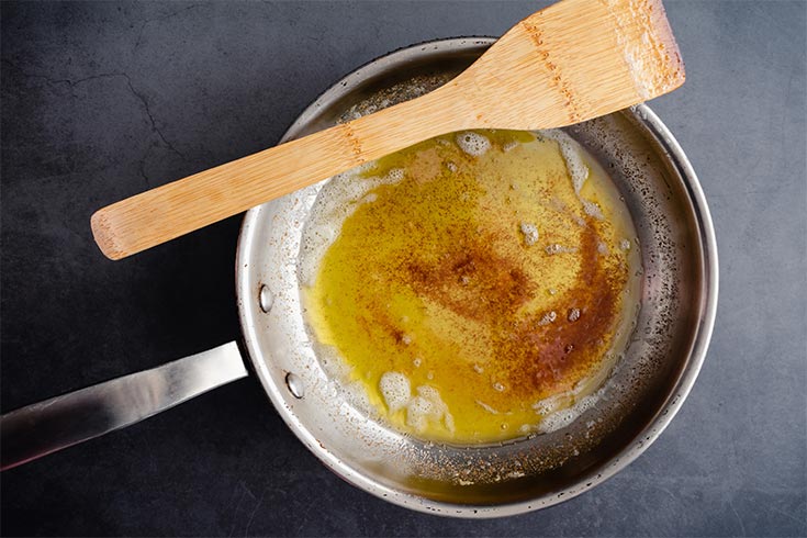 A skillet with browned butter in it. A wood spoon rests on the edge of the skillet.