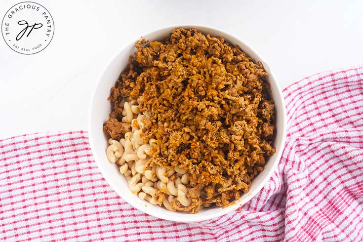 Meat added to cooked noodles in a white mixing bowl.