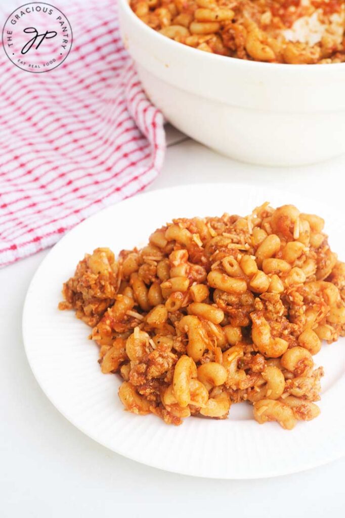 A white plate sits in front of a serving bowl. Both are filled with chili mac.