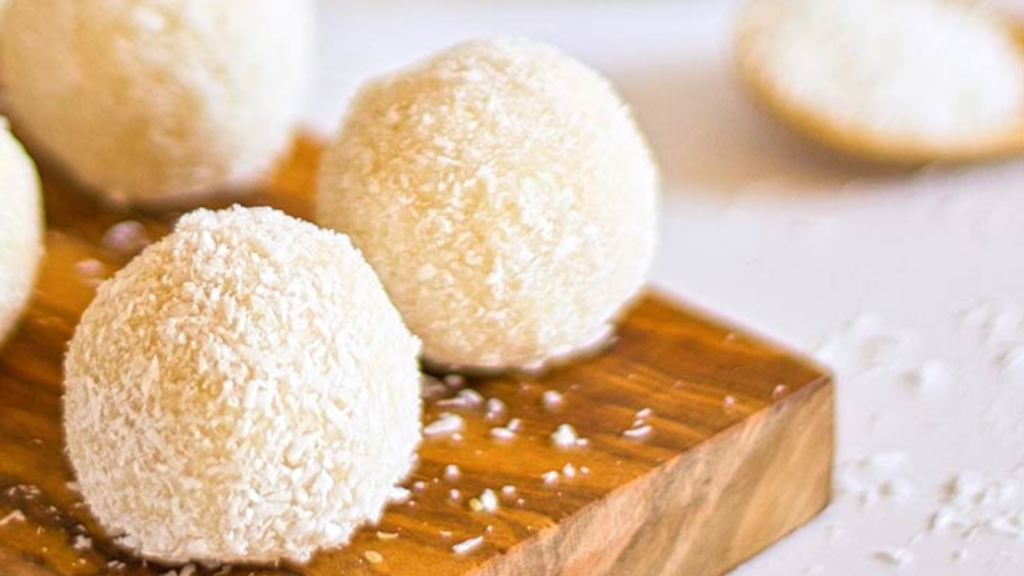 Coconut balls laying on a wood cutting board.