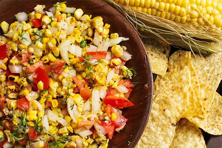 An overhead view of a wood bowl filled with corn salsa.
