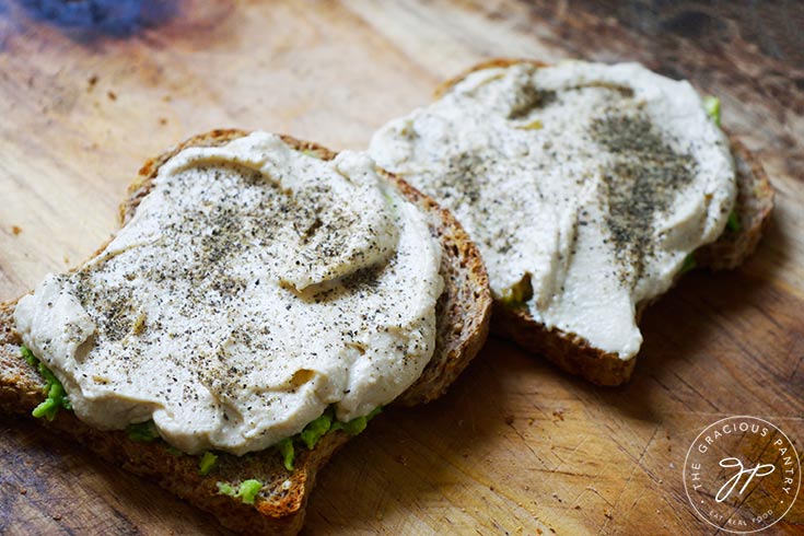 Two slices of Hummus Avocado Toast lay on a cutting board.