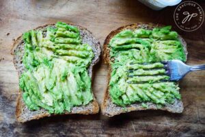 Smashing avocado onto two slices of toasted bread.