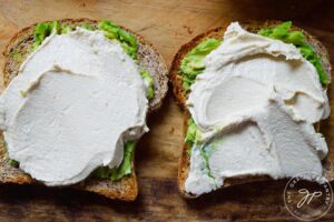 Hummus spread across the top of two slices of toast with smashed avocado on them.