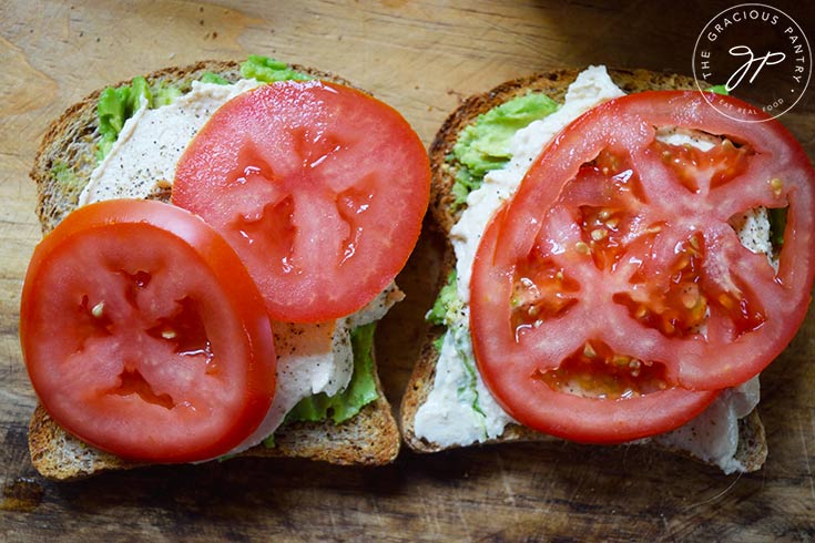 Fresh tomato slices added to two slices of Hummus Avocado Toast.