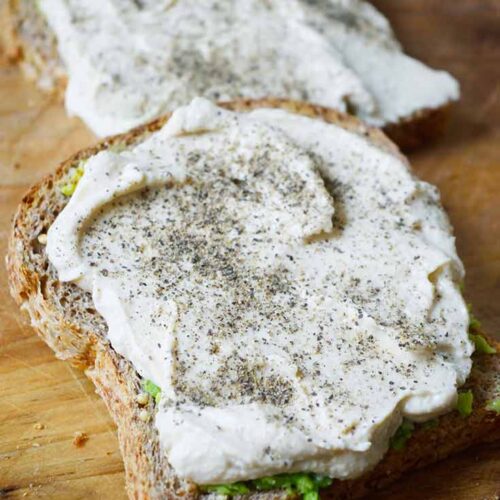 An up close view of two slices of Hummus Avocado Toast on a wood cutting board.