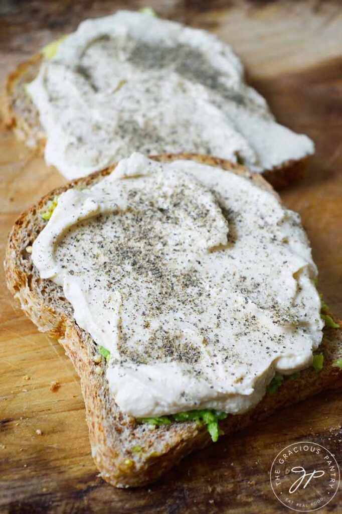 An up close view of two slices of Hummus Avocado Toast on a wood cutting board.