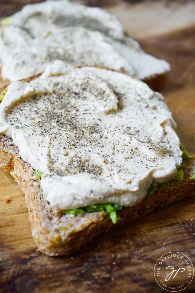 A side view of two slices of Hummus Avocado Toast laying on a cutting board.