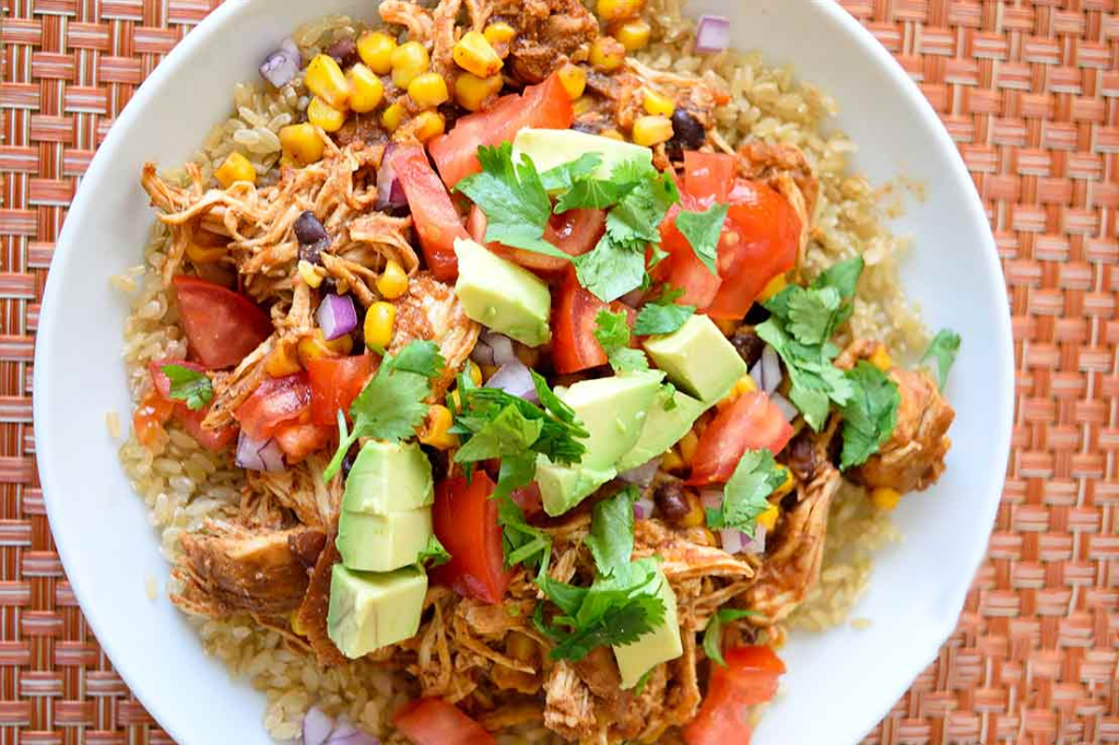 An overhead view of a white bowl filled with instant pot Mexican chicken topped with fresh tomatoes, avocado and cilantro.