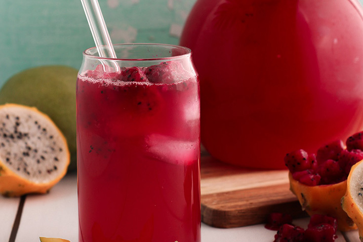 A glass of man dragon fruit lemonade with a glass straw and chunks of dragon fruit in it.