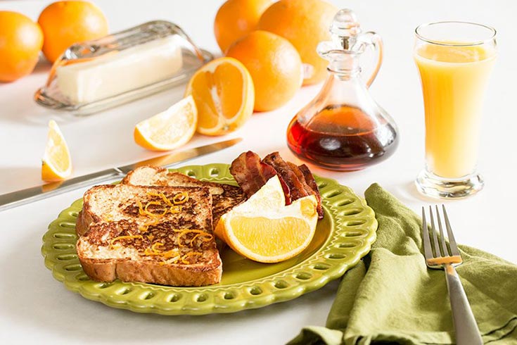 A green plate hols two slices of Mississippi coast French toast and some bacon.