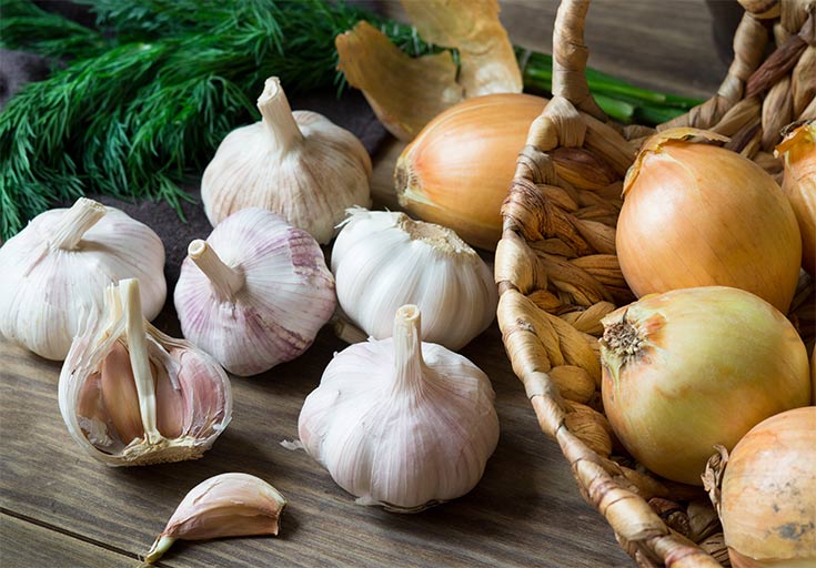 Onions and garlic cloves gathered on a wood table.