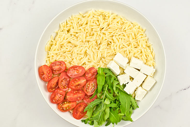 Cut feta added to orzo in a white mixing bowl.