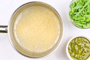 Orzo added to a pot of water sitting on a white surface.