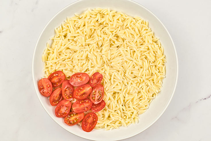 Cut tomatoes added to orzo in a mixing bowl.