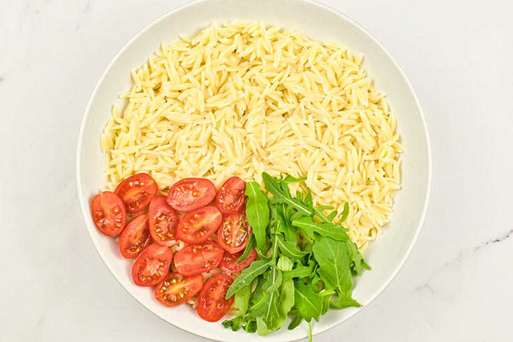 Fresh arugula added to orzo in a mixing bowl.