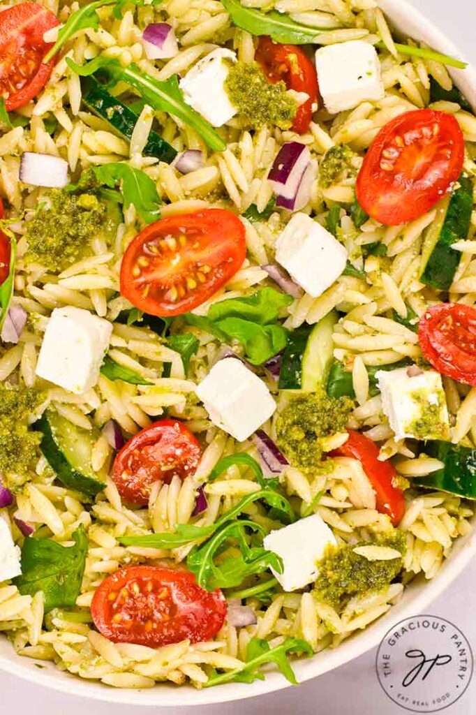 An up close view of a white bowl filled with Orzo Salad With Pesto.