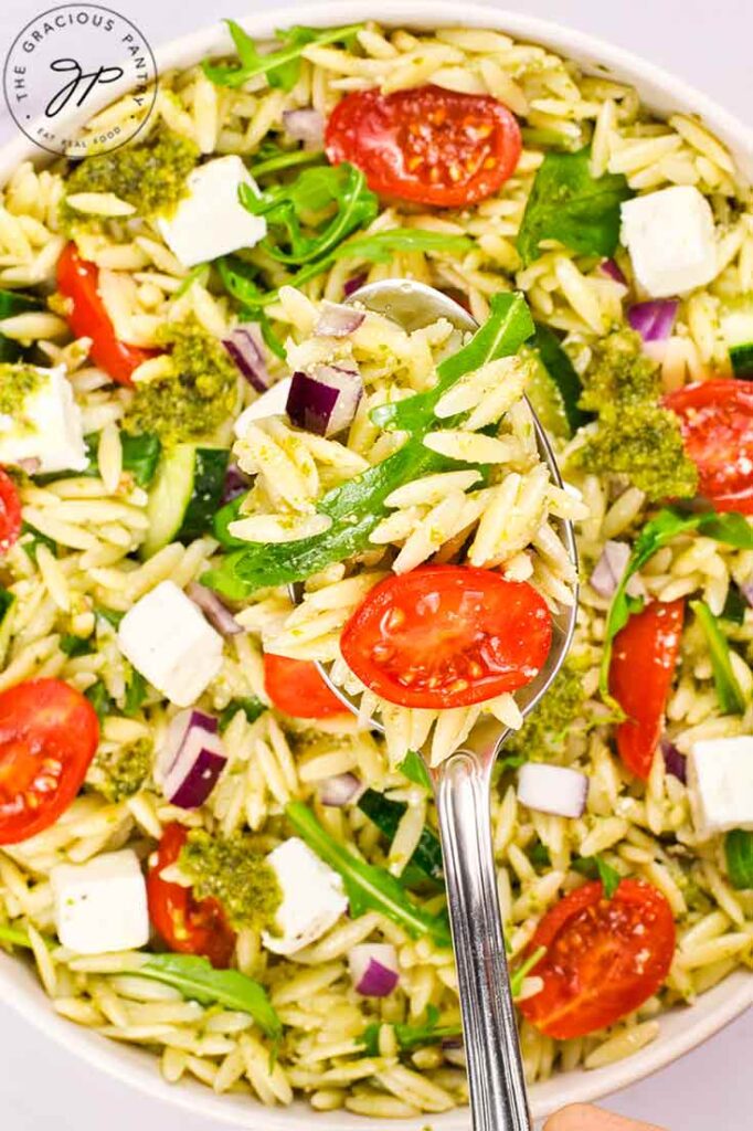 A spoon lifts some Orzo Salad With Pesto out of a bowl.