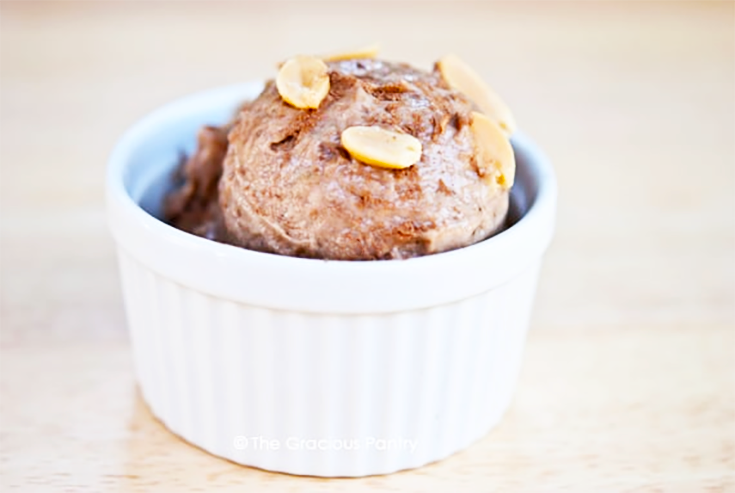 A scoop of chocolate peanut butter ice cream in a small white bowl, garnished with fresh peanuts.