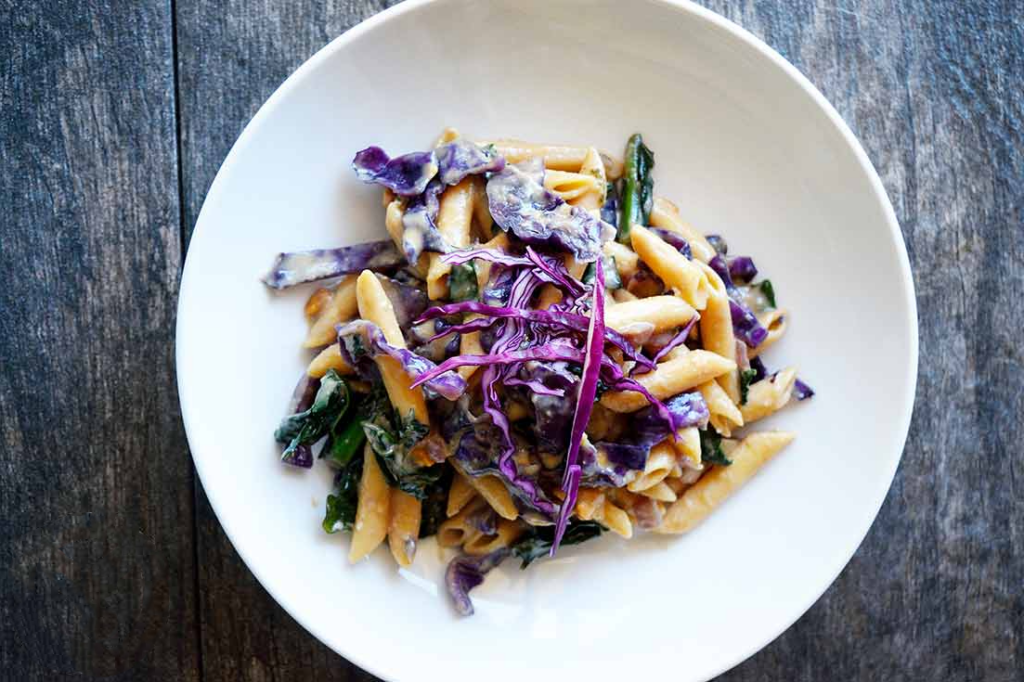 An overhead view of a white bowl partially filled with red cabbage peanut pasta.