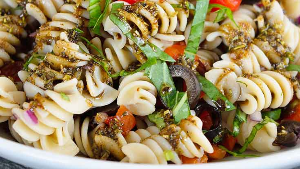 A closeup of a white bowl filled with rustic Italian pasta salad.