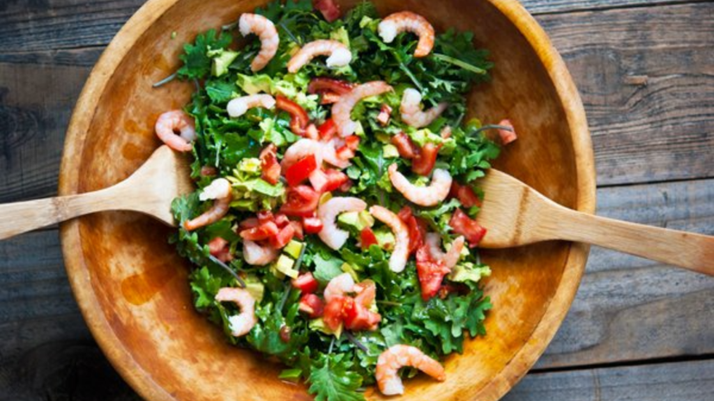 An overhead view of a large wood salad bowl filled with shrimp and kale salad.