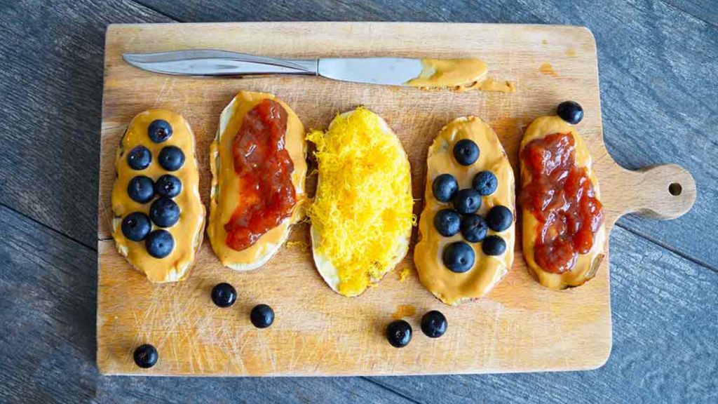A row of five slices of sweet potato toast with different toppings on them, laying on a cutting board.