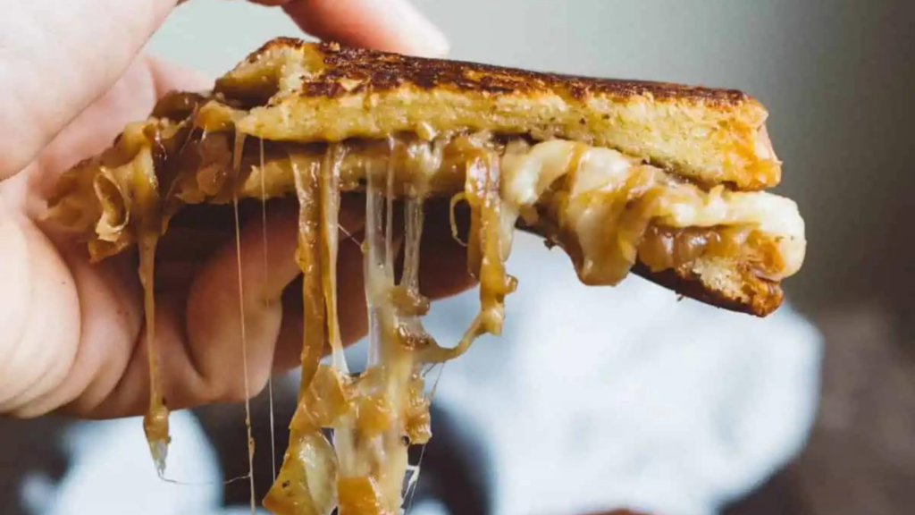 A hand holds a french onion grilled cheese sandwich as the cheese drips down.