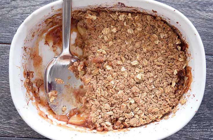 An overhead view of a partially eaten apple crisp in a white casserole dish.