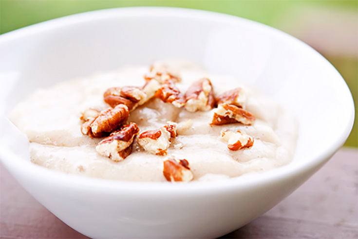 A side view of a white bowl filled with banana pudding and topped with chopped nuts.
