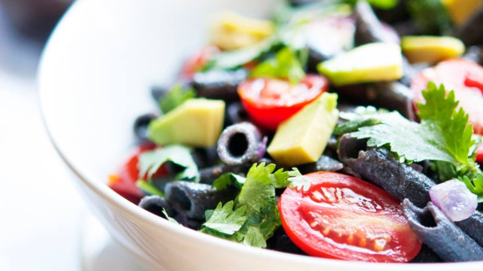 An up close shot of a white bowl filled with black bean pasta.