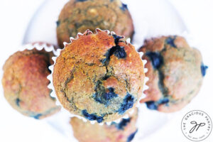 An overhead view of a pile of Blueberry Corn Muffins on a white plate.