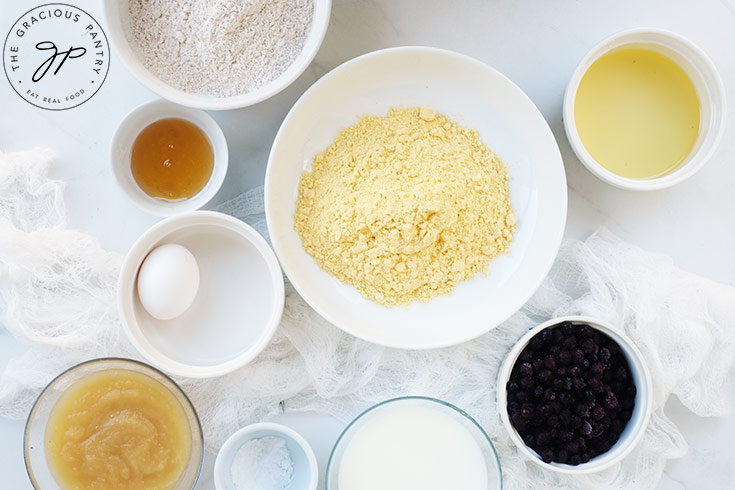 Blueberry Corn Muffins Recipe ingredients on a white surface in individual bowls.