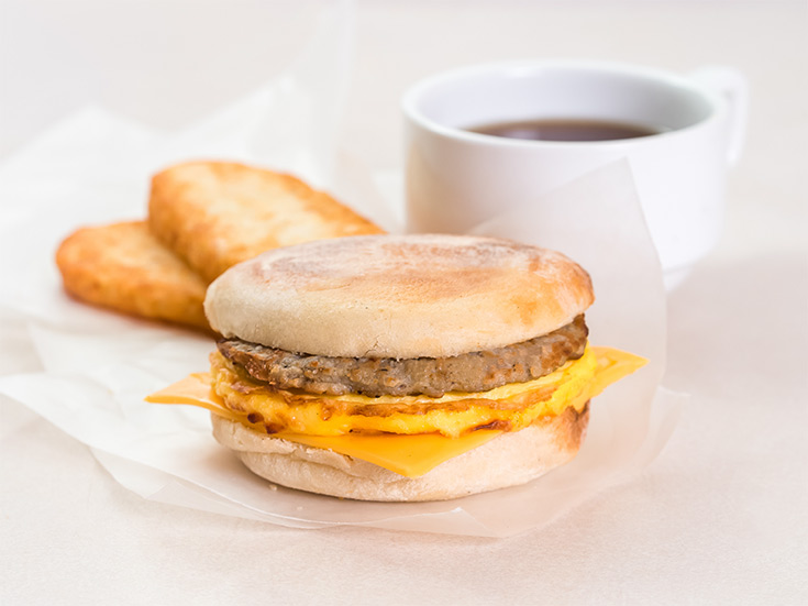 A breakfast sandwich on parchment paper with hash browns and a cup of coffee.