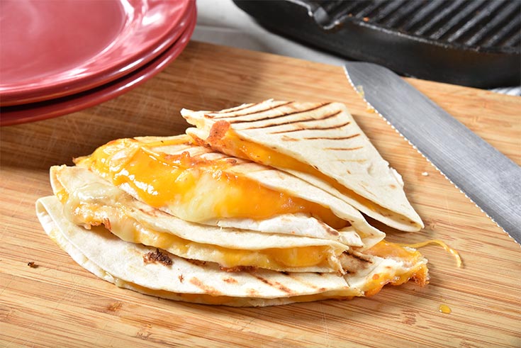 Four cheese quesadilla quarters stacked on a wooden surface.