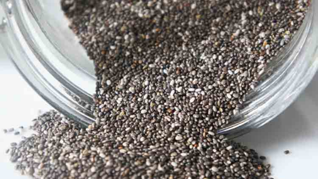 A tipped over glass jar of chia seeds. The seeds are spilling out of the jar.