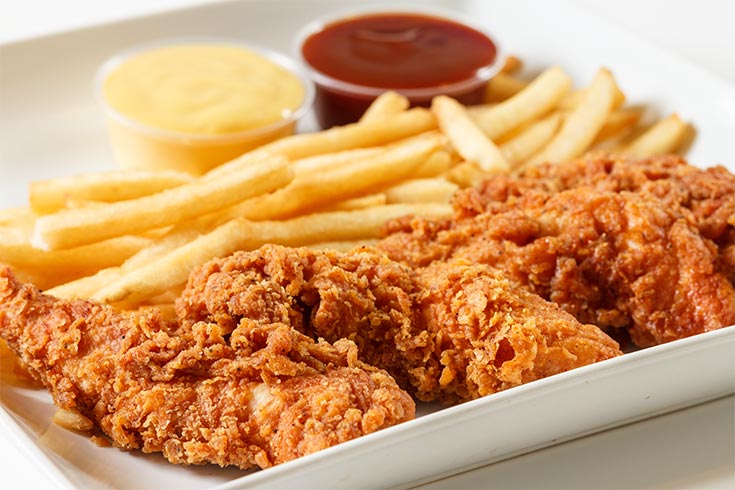 A white plate holds chicken tenders, french fries and two small cups of ketchup and mustard.