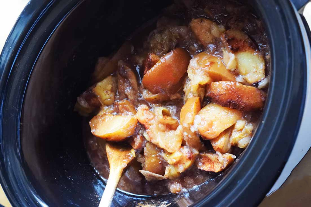 A slow cooker crock half filled with cinnamon apples.