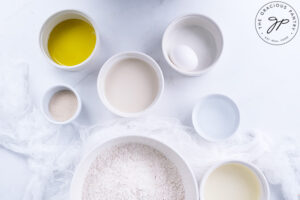 All the ingredients for Homemade Cinnamon Rolls in individual white bowls sitting on a white surface.