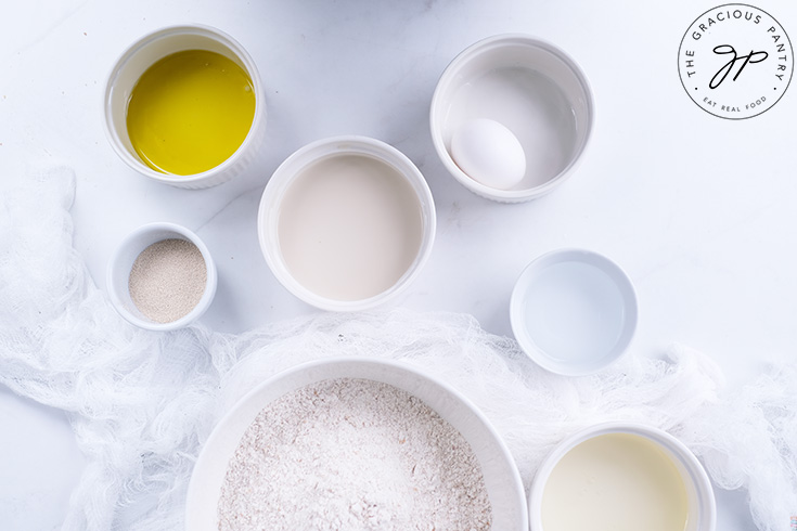 All the ingredients for Homemade Cinnamon Rolls in individual white bowls sitting on a white surface.