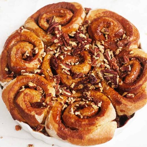 Baked cinnamon rolls topped with chopped pecans and honey glaze.