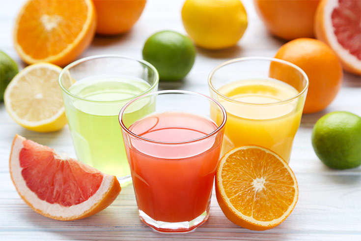 A collection of cut citrus and three glasses of citrus juice.