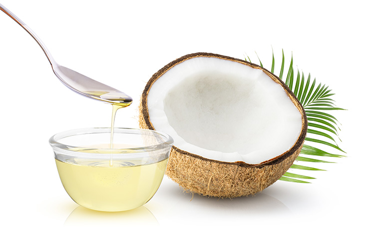 Coconut oil in glass bowl and coconut fruit with green leaves isolated on white background.